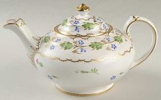 a white tea pot with blue flowers and gold trimmings on the top, sitting in front of a white background