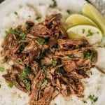 shredded beef and rice on a plate with lime wedges