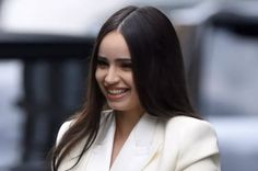 a woman in a white suit smiles as she walks down the street with her hand on her hip