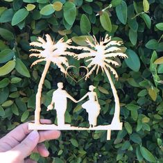 a person holding a paper cutout of two people under a palm tree