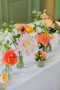 several vases with flowers are lined up on a white tableclothed table cloth