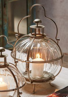 two clear glass lanterns with candles in them on a table next to an open book