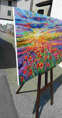 an easel with a painting on it sitting in front of a house and building