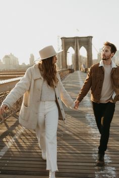 a man and woman walking across a bridge holding hands