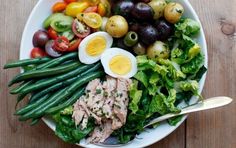 a bowl filled with salad and eggs on top of a wooden table