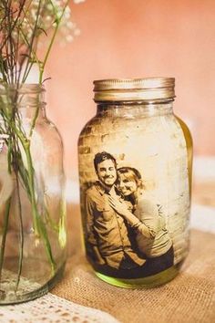 a jar with a photo on it next to a vase filled with flowers and grass