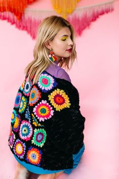 a woman sitting on the ground wearing a black and multicolored ponchy