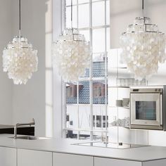 two chandeliers hanging over a kitchen counter next to a microwave oven and window