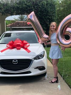 a woman standing next to a white car holding balloons