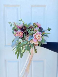 a bridal bouquet in front of a white door with pink flowers and greenery