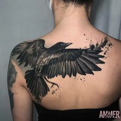 the back of a woman's shoulder with a black bird tattoo on her chest