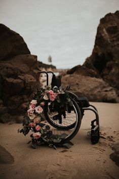 a wheel chair with flowers on it sitting in the sand near some rocks and water