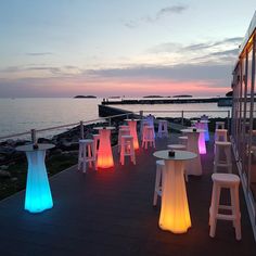 there are many chairs and tables on the deck by the water at sunset or dawn