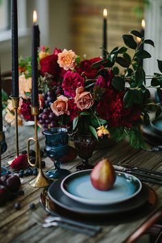 the table is set with plates, candles and flowers in blue vases on it