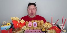 a man sitting in front of a table full of fast food and fries, with his mouth wide open