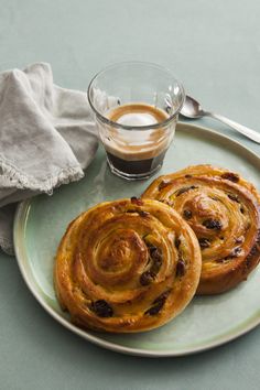 two cinnamon rolls on a plate next to a cup of coffee