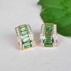 Immerse yourself in the allure of 18K Gold Baguette Tsavorite Art deco Pyramid Diamond Stud Earrings—a mesmerizing masterpiece designed to captivate with its vibrant green radiance. The baguette-cut Tsavorite gemstones take center stage, meticulously calibrated and cut by skilled lapidary artists. Encased in trapezoid gold settings, they exude elegance, creating a captivating visual. Art Deco Stud Earrings, Elegant Green Baguette Cut Earrings, Green Baguette Diamond Jewelry For May Birthstone, Green Baguette Cut Earrings For Formal Occasions, Green Baguette-cut Art Deco Jewelry, Green Baguette Cut Earrings For Gifts, Diamond Stud Earrings, Baguette Cut, Diamond Stud