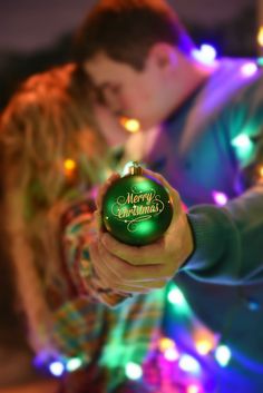 a man and woman kissing while holding a christmas ornament in front of lights