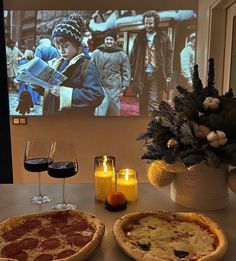 two pizzas sitting on top of a table next to glasses of wine and candles