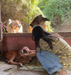 a woman kneeling down petting a baby goat