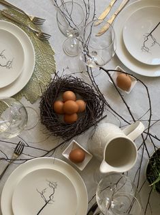 the table is set with white dishes and place settings, including eggs in a bird's nest