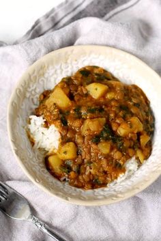 a white bowl filled with stew and rice on top of a gray towel next to a fork