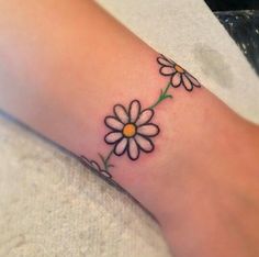 a small daisy tattoo on the foot of a woman's leg, with an arrow in