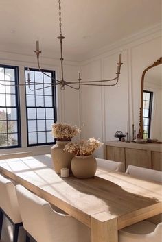 a dining room table with chairs and vases on it in front of two windows