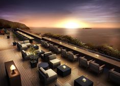 an outdoor seating area overlooking the ocean at sunset or sunrise with tables and chairs set up on wooden planks