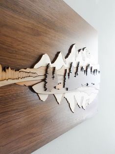 a wooden wall hanging with mountains and trees cut out of it's sides on a white wall