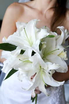 a woman in a wedding dress holding a bouquet of white lilies and greenery