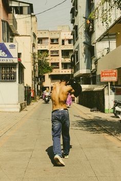 a shirtless man walking down the middle of a street with buildings in the background