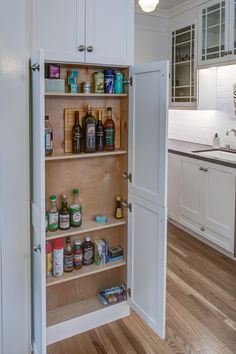 an open cabinet in the middle of a kitchen with lots of spices and condiments