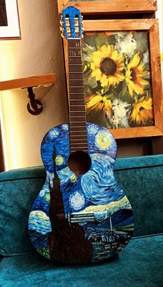 a guitar sitting on top of a blue couch next to a painting and a framed picture