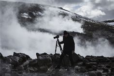 a man standing on top of a rocky hillside next to a camera and tripod