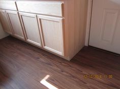 an empty kitchen with white cabinets and wood flooring on the side of the door