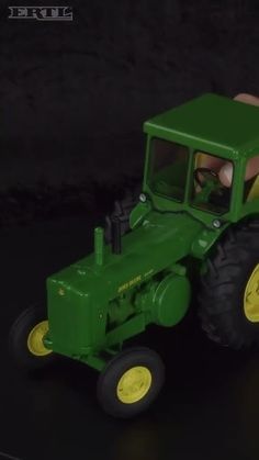 a green toy tractor sitting on top of a black floor next to a person's hand