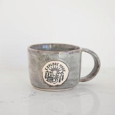 a coffee cup with an emblem on it sitting on a white countertop next to a wall