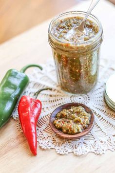 a jar of chili paste next to two peppers on a doily with a spoon in it