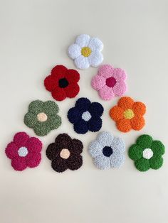 six crocheted flowers are arranged on a white surface with one flower in the center