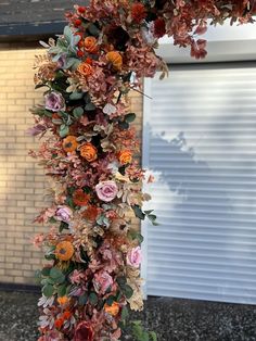 an arrangement of flowers is hanging from a pole in front of a brick wall and garage