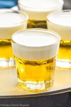 four shot glasses filled with liquid sitting on top of a metal tray next to each other