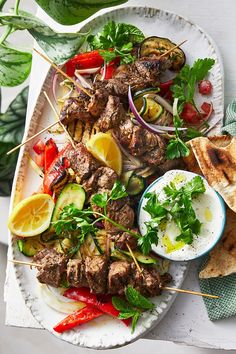 a platter filled with meat, vegetables and pita bread on skewers