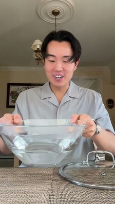 a man holding a glass bowl with his mouth wide open while standing in front of a table