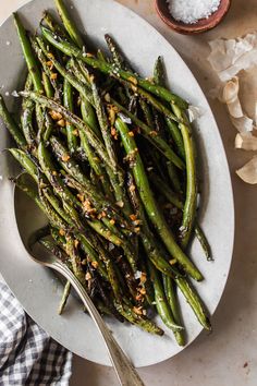 a white plate topped with green beans covered in seasoning next to a bowl of salt and pepper