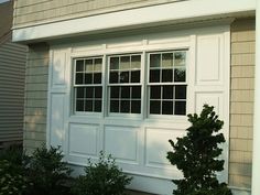 a white garage door with two windows on the side of it and bushes in front