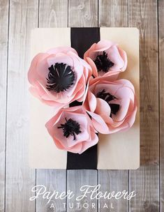 three pink flowers sitting on top of a piece of paper next to a black ribbon