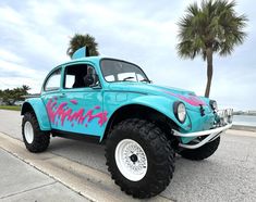 a blue monster truck with pink graffiti on it's front wheels parked next to a palm tree