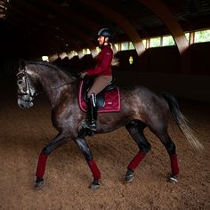 a woman riding on the back of a brown horse in an indoor arena at night