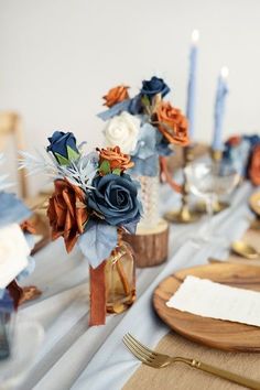 the table is set with blue and orange flowers in vases, candles, and napkins